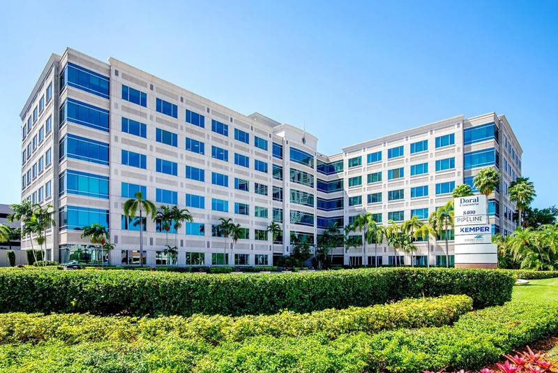 A low-rise office building with a glass frontage and palm trees under a clear sky